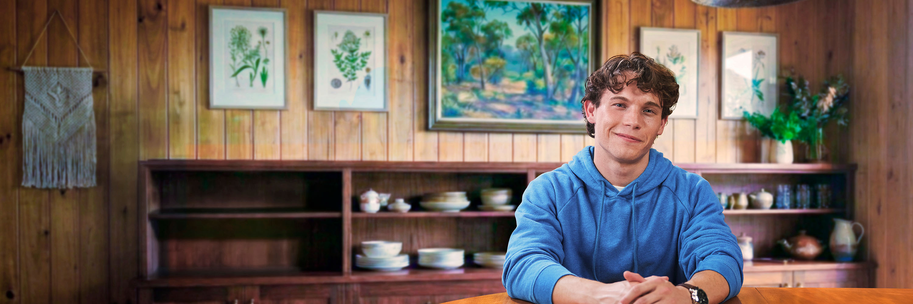 Young man sitting in a kitchen wearing a blue jumper