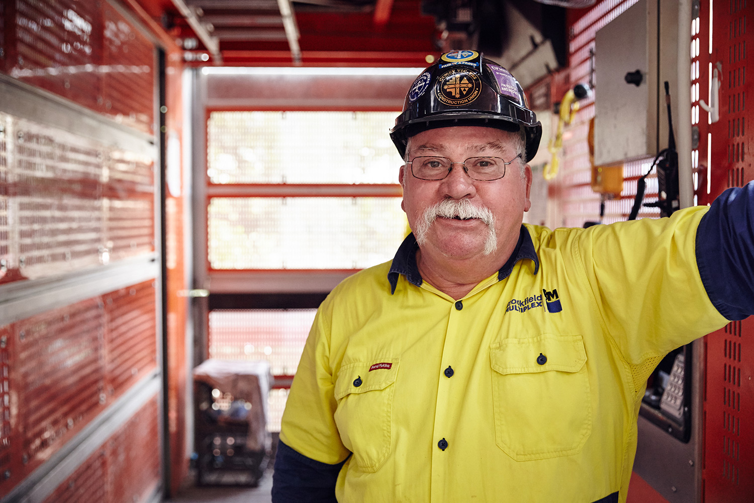 Older man wearing a high visibility yellow shirt and a blue hard hat
