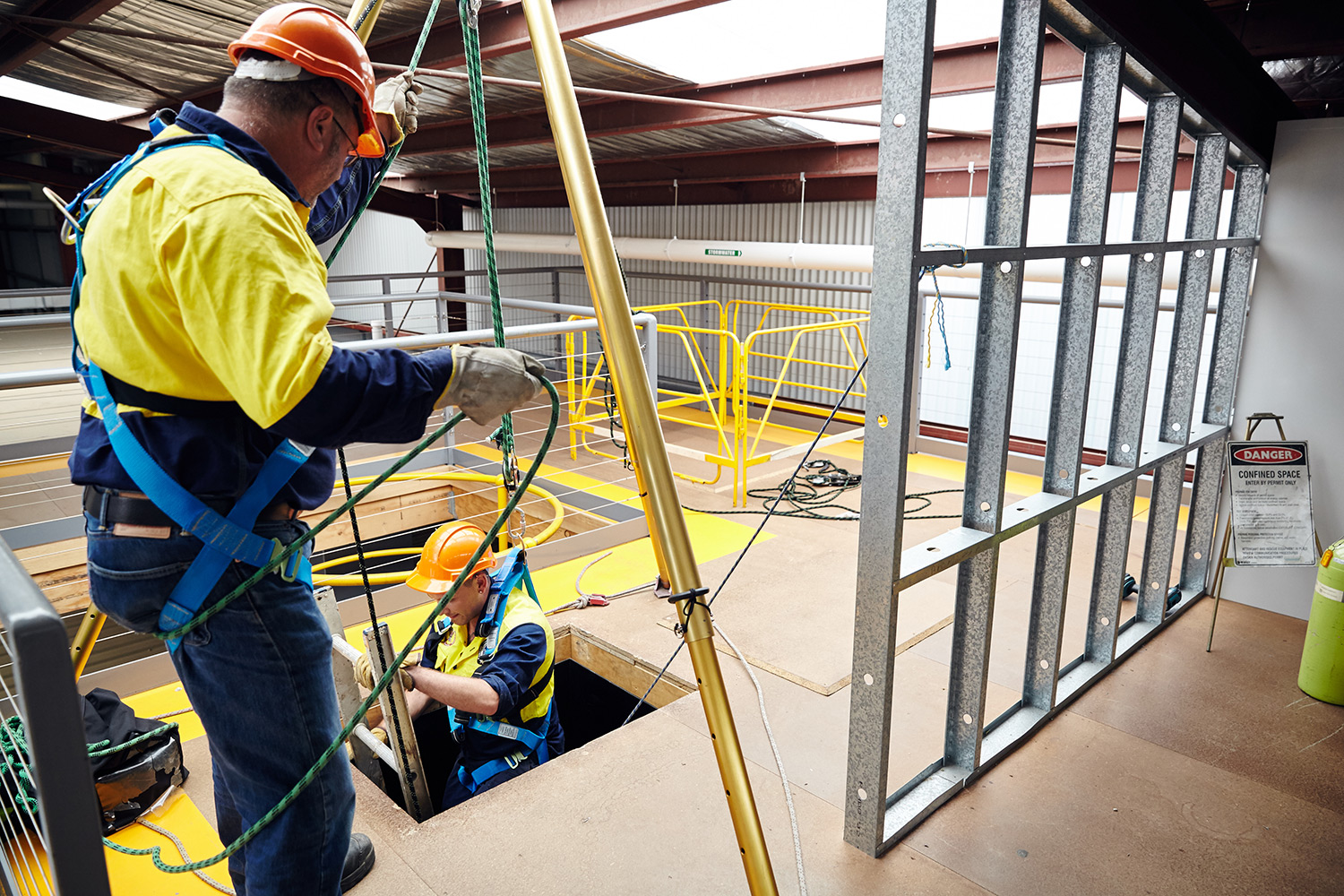 Two males workers in building site lowering themselves with safety harness
