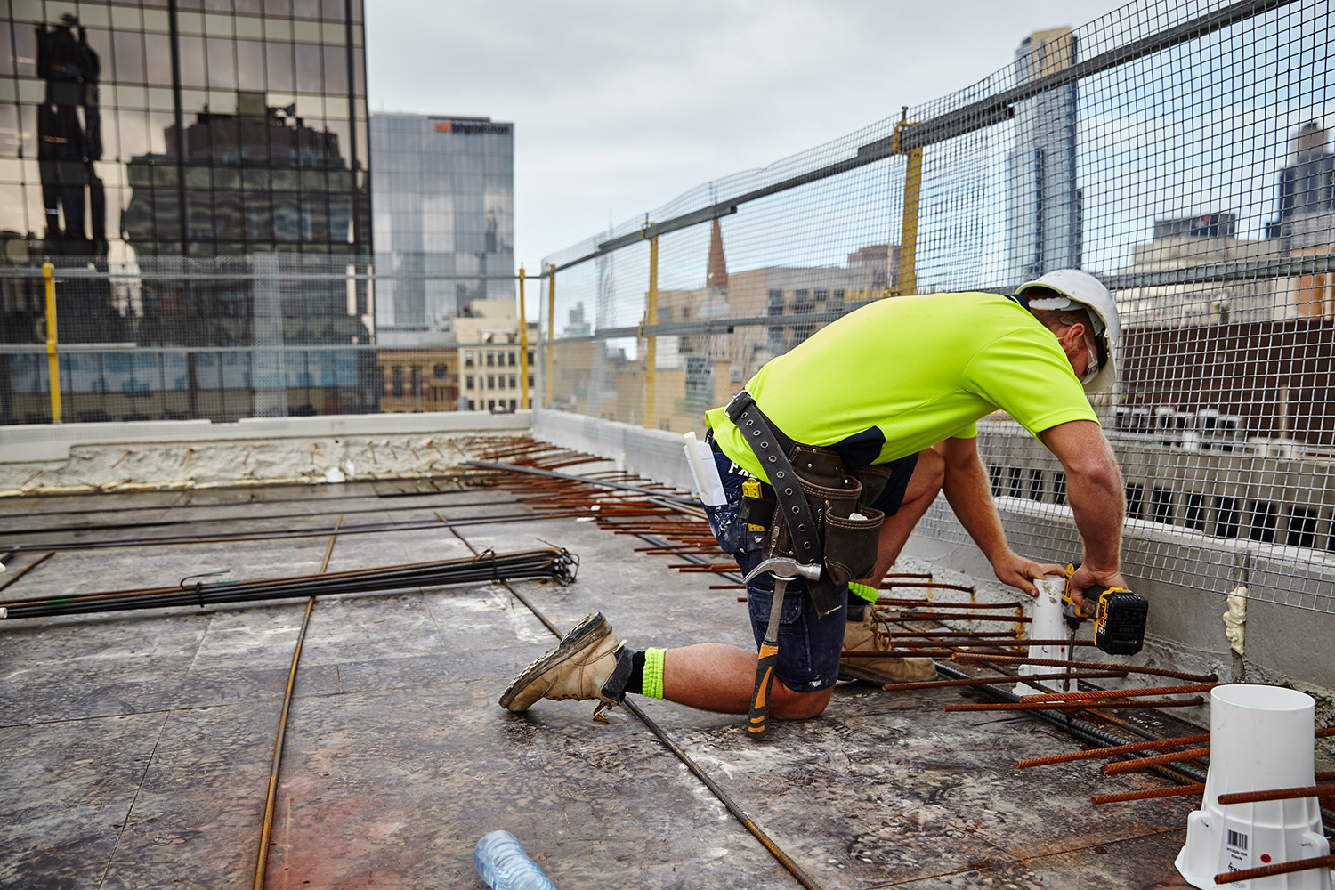 Male construction worker in hi vis on a roof top drilling in the ground