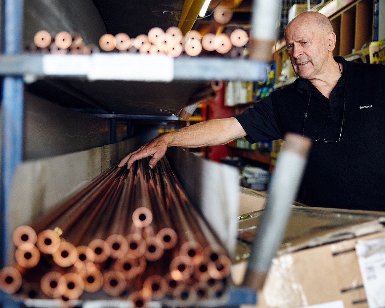 Man reaching for copper pipes off a shelf
